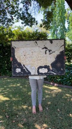 a woman standing in the grass holding up a sign with an old world map on it