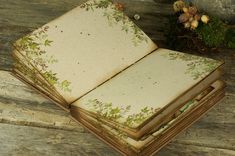 an open book sitting on top of a wooden table next to some flowers and plants