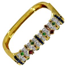 A unique, modern, hinged cuff bracelet, with a slightly squared off design. This colorful piece tapers in width from just under half an inch at the top, down to 1/4 of an inch at the base. Crafted in 18K yellow gold, the top has the appearance of a cylinder of diamonds accented by bands of emerald, ruby, and sapphire. The outer walls of this piece feature a detailed pattern resembling scales or cobblestones. There are a total of 64 round brilliant cut diamonds weighing a combined weight of approximately 2.25ct of overall G color and VS2 clarity. The colored stones added to the backdrop of diamonds weigh a total of approximately 5.75ct. Stamped 750 and 18K. Inside circumference measures 7 inches. Gross weight 57.6 grams. Ruby And Sapphire, Ruby Sapphire, Top Down, Bracelets And Charms, Round Brilliant Cut Diamond, Vintage Watches, Round Brilliant, Cuff Bracelet, Antique Jewelry