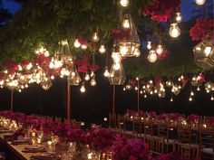 the tables are set with candles, flowers and lanterns hanging from the trees above them