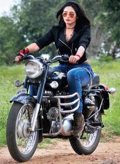 a woman riding on the back of a motorcycle down a dirt road