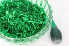 a bowl filled with green shredded grass next to a plastic spoon on a white surface