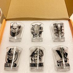 six shot glasses in a cardboard box with the lids open and logos printed on them