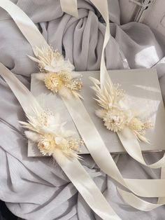 two pieces of white ribbon with flowers on them sitting on top of a cloth bag