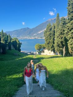 three girls are walking up some steps towards the water