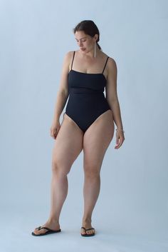 a woman in a black one piece swimsuit and flip flops is posing for the camera