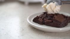 a spoon scooping ice cream over a piece of chocolate cake on a white plate