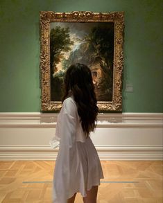 a woman standing in front of a painting with her back to the camera and looking at it