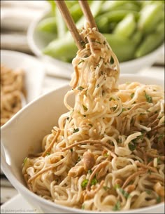 a bowl full of noodles with chopsticks sticking out of the top and green beans in the background