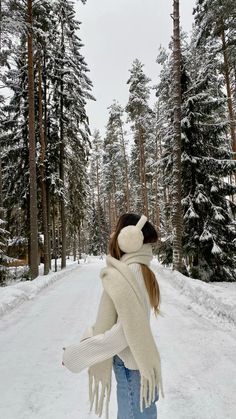 a woman standing in the middle of a snow covered forest wearing a scarf and mittens