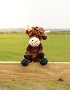 a small stuffed cow sitting on top of a wooden fence in front of a green field