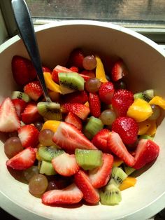 a white bowl filled with lots of different types of fruit on top of a window sill