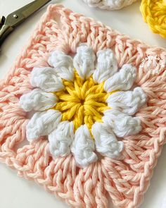 a crocheted square with a flower on it next to scissors and yarn balls