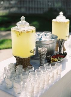 there are many glasses on the table with drinks in them and ice buckets next to it