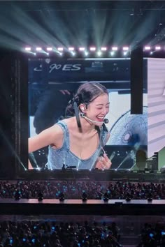 a woman with a headset on in front of a large screen at a concert