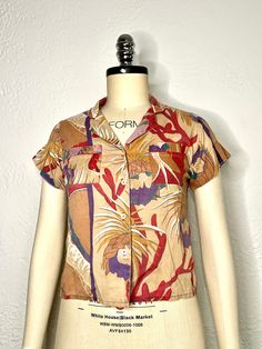 Relax and look cool in this classic vintage 90s Hawaiian collard blouse with an Orchid design in beige, purple, red, green, & white. Showcasing a simple motif of Orchid Flowers. This Hawaiian-made shirt is sewn with two front breast pockets, button up closure, and single stitched short sleeves in a soft cotton fabric. This is an easy Hawaiian or summer shirt choice for just about any day. Measurements: Armpit to armpit: 18 inches Back length: 23 inches Vintage Cotton Printed Short Sleeve Shirt, Vintage Printed Cotton Short Sleeve Shirt, Casual Multicolor Blouse With Vintage Print, Multicolor Collared Top With Retro Print, Cotton Tops With Retro Print And Camp Collar, Multicolor Retro Print Button-up Top, Cotton Top With Retro Print And Camp Collar, Casual Short Sleeve Blouse With Retro Print, Cotton Button-up Blouse With Graphic Print