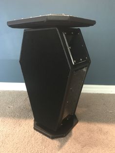 a large black speaker sitting on top of a carpeted floor next to a blue wall