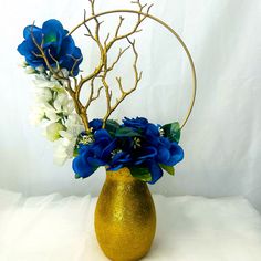 a gold vase filled with blue and white flowers on top of a white tablecloth