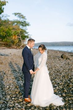 a bride and groom standing on rocks near the ocean