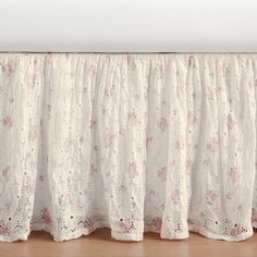 a white bed skirt with pink flowers on it and a wooden floor in the background