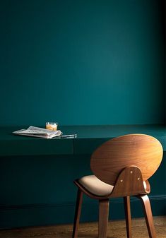 a wooden chair sitting in front of a green wall next to a table with a cup on it