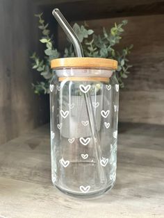 a glass jar with a straw in it on a wooden table next to a plant