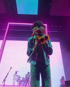 a person standing in front of a stage with flowers on their head and microphones