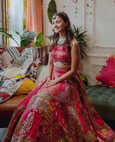 a woman in a red and gold bridal gown sitting on a couch next to a potted plant