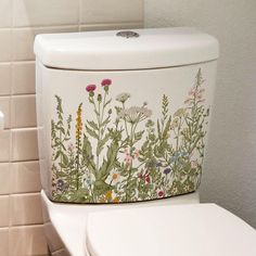 a white toilet with flowers painted on the lid and tank cover is in a bathroom