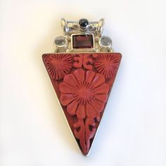 "Cinnabar, with a lovely floral design, has been bezel set in 925 Sterling Silver in this gorgeous bright red pendant.  Cinnabar is a resin that comes from the Laq tree in Asia. Once hardened, skilled artisans carve wonderful patterns in the medium.  This pendant also features a rectangle of Garnet, two rounds of Moonstone and a round of Black Star Diopside adorns the tube bale. The total length of this piece is 1 3/4\" long. Designed by Marianna and Richard and handmade by Balinese Artisans an Red Cabochon Spiritual Jewelry, Spiritual Red Cabochon Jewelry, Red Multi-stone Jewelry Gift, Red Multi-stone Jewelry As Gift, Red Multi-stone Jewelry For Gifts, Unique Red Cabochon Jewelry, Artisan Red Carved Jewelry, Red Carved Jewelry Gift, Red Carved Jewelry For Gifts