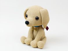 a crocheted dog sitting on the ground with a tag around its neck and eyes