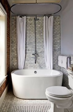 a white bathtub sitting next to a toilet in a bathroom under a window with curtains