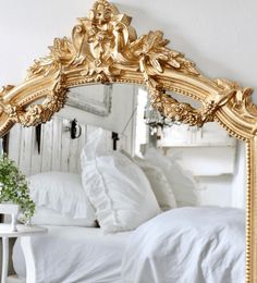 a large gold mirror sitting on top of a white table next to a bed and pillows