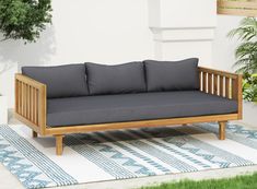 a wooden couch sitting on top of a rug next to a potted green plant