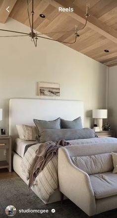 a large bed sitting under a wooden ceiling next to a white couch and table with two lamps on it