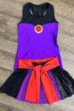 a purple and black dress with red ribbon around the waist on a wooden floor,