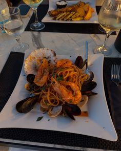 a white plate topped with pasta and clams on top of a table next to wine glasses