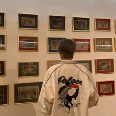 a person standing in front of a wall with framed pictures on it and wearing a jacket