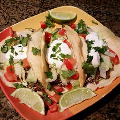 three tacos on a plate with limes and tomatoes