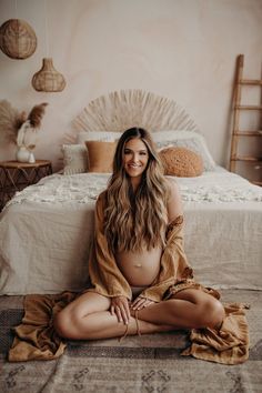 a pregnant woman sitting on the floor in front of a bed wearing a robe and smiling