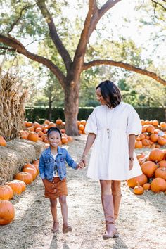 a woman holding the hand of a little boy in front of pumpkins