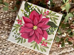 a painting of a pink flower with green leaves and berries on a woven mat next to some plants