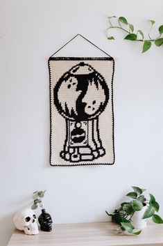 a crocheted wall hanging with two cats and a dog on it, next to a skull