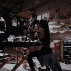 a woman sitting on a chair in front of a bike and other parts hanging from the ceiling