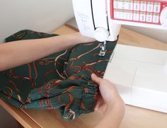 a woman is using a sewing machine to sew on her green fabric with red and white numbers