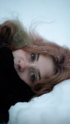 a woman is laying in the snow with her eyes wide open and hair blowing back