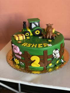 a birthday cake decorated with farm animals and tractor on top of a table next to a pink wall