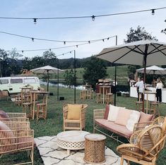 an outdoor seating area with wicker chairs and umbrellas on the grass next to a lake