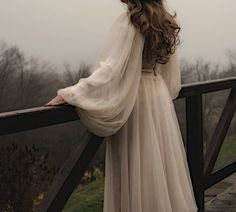 a woman is standing on a bridge with her back to the camera, wearing a long white dress