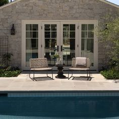 two chairs sitting in front of a swimming pool next to a stone building with french doors